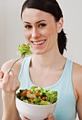 Frau isst Blattsalat mit Tomaten