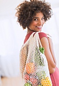 Junge Frau trägt Einkaufstüte mit Gemüse und Obst