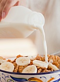 Close up of hand pouring milk into bowl of cereals