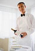 Smiling waiter holding champagne bottle and looking at camera