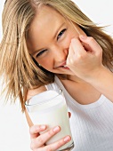 Junge Frau hält verschmitzt lachend ein Glas Milch in der Hand