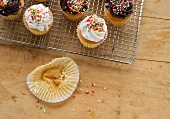 Cupcakes auf einem Abkühlgitter; daneben eine leergegessene Papiermanschette