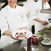 Chefs preparing food in kitchen, women showing dessert
