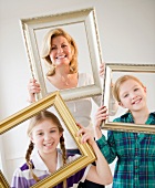 Mutter mit zwei Töchtern schauen durch hochgehaltene Bilderrahmen