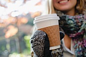 Frau mit Handschuhen hält Plastikbecher mit Kaffee