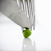Close up of knife, fork and green pea, studio shot