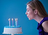 Young woman blowing candles on birthday cake, studio shot