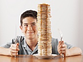 Young boy sitting behind a tall stack of pancakes