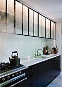 Küchenzeile mit Marmor Arbeitsplatte, schwarzen Unterschränken und Glastüren an Hängeschränke