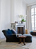 Ethnic-style side table next to blue armchair with matching footstool and scatter cushions in front of fireplace in grand living room with tall latticed windows
