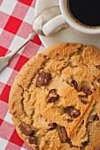 A chocolate chip cookie and a cup of coffee on a red gingham tablecloth
