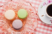 Pastel-coloured macaroons on a crystal plate next to a cup of coffee