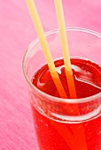 A glass of strawberry lemonade with drinking straws against a pink background