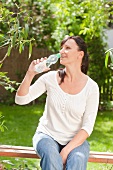 Frau trinkt Wasser auf einer Gartenbank