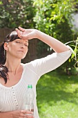 Frau mit Wasserflasche bei sommerlicher Hitze im Garten