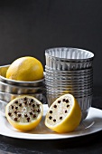 Lemons with cloves and muffin tins on a white plate