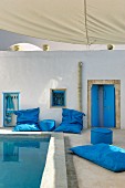 North-African-style courtyard with blue floor cushions and pouffes around pool