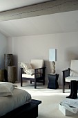 Table lamp on modern stool flanked by armchairs against grey well in bedroom with wood-beamed ceiling