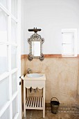 Marokkanisches Bad in sanften Erdtönen mit verziertem Spiegel, Holz-Waschtisch, marmoriertem Wandbereich und Terracottaboden