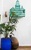 Palm in blue-painted pot and clay vessel below old, Oriental bird cage in corner