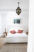 Simple bed with wood-panelled headboard and bright scatter cushions below Oriental pendant lamp