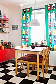 Dining table in kitchen with chequered floor & colourful curtains