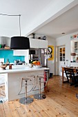 Pendant lamps with black lampshades above modern island counter with designer barstools on wooden floor
