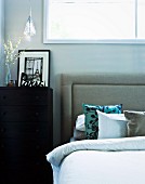 Black and white photo of Paris on black chest of drawers next to double bed with upholstered headboard and silk scatter cushions