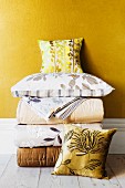 Folded, elegant quilts, bed linen and scatter cushions against golden yellow wall