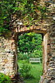 Alte, eingewachsene Klostermauer mit Durchgang in romantischen Garten mit verwitterter Gartenbank