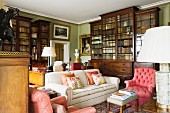 Upholstered chairs and sofa in front of traditional bookcases in library of English country house