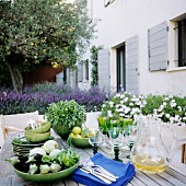 Auberginen, Kräuter und Geschirr auf Holztisch vor modernem mediterranem Ferienhaus; blühender Lavendel im Hintergrund