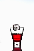 Ice cube falling into a glass of Campari