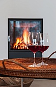 Two glasses of red wine on a table in front of a fireplace