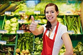 Germany, Cologne, Young woman showing thumbs up in supermarket, smiling, portrait