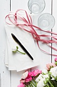 Ranunkelblüten, weiße Papiertüten, Stift, Geschenkband und Gläser auf weißem Holzuntergrund