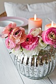 Ranunculus posy in shiny silver vase in front of lit candles