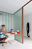 Lady at a modern desk in an open corner with glass walls and a view of a wardrobe in the hallway