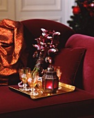 A tray with wine glasses, a hurricane lamp and orchids on a red sofa (Christmassy)