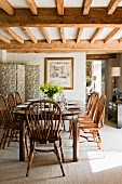 Country-house-style dining room with tasteful wooden furniture below wood-beamed ceiling; floral screen in corner