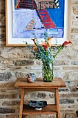 Colourful modern painting on rustic stone wall; magnificent bouquet of calla lilies on small console table