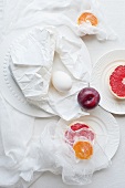 Grapefruit, Pflaume und Ei auf weissen Tellern und Mulltuch