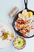 Prawn skewers with lemon wedges in a frying pan, alongside string, rice noodles and salad