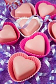 pink love heart shaped chocolates in pink cake covers with purple party streamers on a purple glittery table top