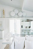 Blick über weiße Kissen und Sitzbank auf weiss lackierte Schild-Sammlung und Ablage über der Tür in weißem Designer Wohnraum