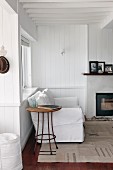 White couch and small side table in peaceful corner of room next to wood-burning stove; photographs in black frames on mantelpiece