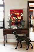 Antique console table below modern painting on white wall; life-size bronze of greyhound in foreground