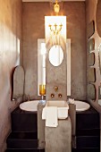 Free-standing concrete column with sink, tap fittings and candle sconce above mirror in front of black platform with sunken bathtub