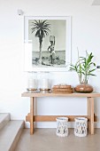 Framed black and white photograph above large lanterns and potted plant on simple console table
