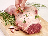 A hand sticking rosemary into a leg of lamb